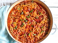 a pan filled with spaghetti and sauce on top of a blue towel next to a wooden table