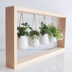 four hanging planters with plants in them on a wooden frame against a white wall