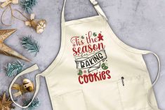 an apron with the words tis the season baking cookies on it next to christmas decorations