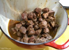 a pot filled with meat and sauce on top of a yellow tablecloth next to a red spatula