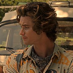 a close up of a person wearing a shirt and looking off into the distance with trees in the background