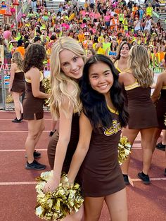 two cheerleaders posing for a photo in front of a crowd