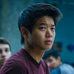 a young man in a maroon shirt stares into the distance with other people behind him