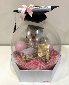 a graduation cap on top of a teddy bear in a glass ball with pink and gold confetti