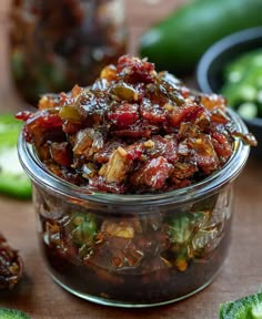 a glass jar filled with pickles on top of a wooden table next to sliced jalapenos