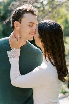 a man and woman kissing each other in front of some trees with their eyes closed