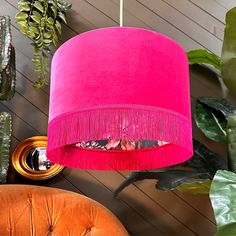 a pink lampshade hanging from a ceiling in a room with plants and other decor