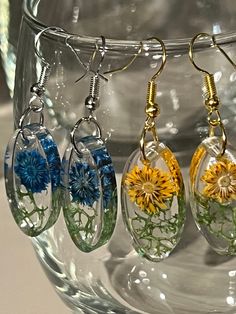 three dandelions are hanging from clear glass earwires with yellow and blue flowers on them