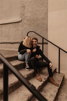 a man and woman are sitting on the steps together smiling at each other as they hug