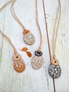 three different necklaces are shown on a white wooden surface, one is decorated with leaves and the other has an orange leaf