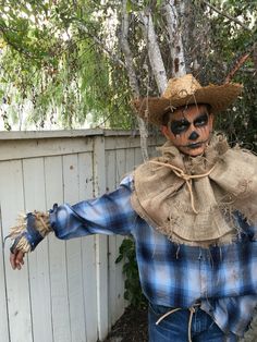 a scarecrow dressed in plaid shirt and cowboy hat standing next to a white fence