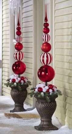 two red and white christmas decorations in urns on the side of a house with snow