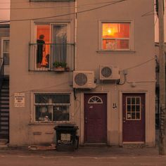 an apartment building with two red doors and a person looking out the window at the street