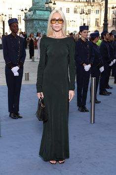 a woman in a long green dress standing on a blue carpet with other people behind her