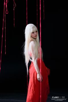 a woman with long white hair and red dress standing in front of pink streamers