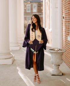 a woman wearing a graduation gown and standing in front of a brick building with columns