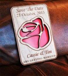 a wooden save the date magnet on top of a brown leather chair with a pink rose