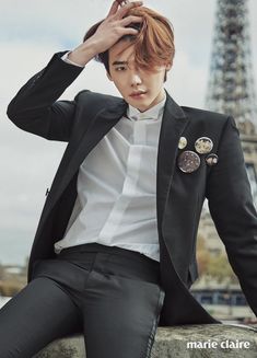 a man in a black suit and white shirt sitting on a ledge with the eiffel tower in the background