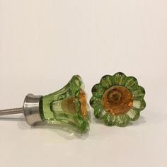 two green glass knobs sitting next to each other on a white surface with a metal hook