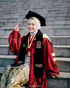 a woman wearing a graduation gown and holding up a red tassel in front of some steps