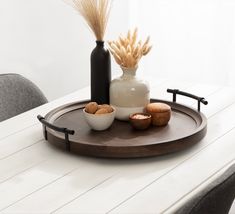 a wooden tray with some nuts and a bottle on it sitting on a dining room table