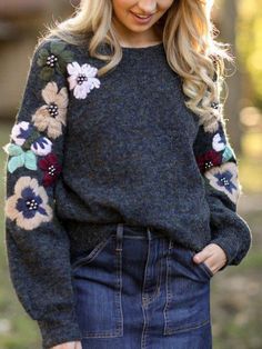 a woman with long blonde hair wearing a black sweater and flowered sleeves is standing in the grass