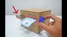 a hand is holding a blue plastic object in front of a cardboard box with money inside