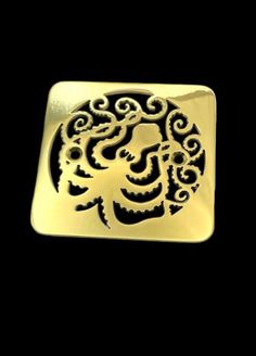 a gold square brooch with an intricate design on the front and back of it