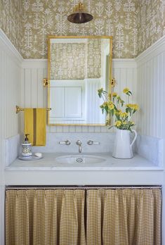 a white sink sitting under a mirror next to a yellow and white wallpapered bathroom