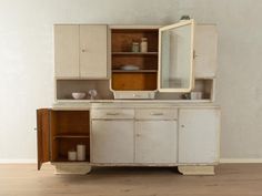 an old white cabinet with a mirror on top and other items in the cupboards