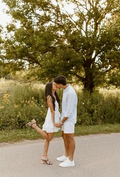 a man and woman kissing in the middle of a road with trees in the background