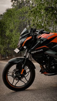 an orange and black motorcycle parked on the side of the road in front of some trees