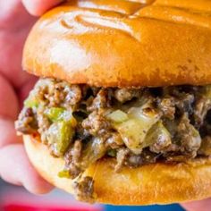 a close up of a person holding a hamburger with meat and vegetables on it's bun