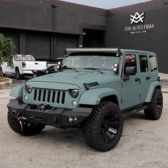 a green jeep is parked in front of the auto firm's building with other cars behind it