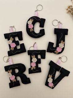 the letters are made out of felt and have pink flowers on them, along with two keychains