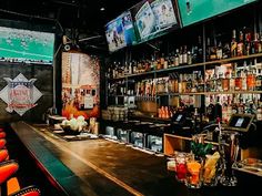 a bar with many bottles and glasses on the counter in front of televisions above it