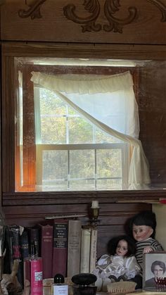 two dolls sitting in front of a window with books on the shelf next to them