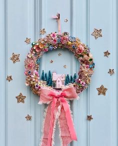 a wreath with a pink bow hanging on the front door, decorated with flowers and stars