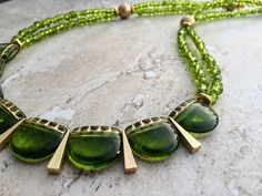 This delicately gorgeous necklace features a bib made using Czech glass beads in fresh green with gold accents interspersed with matte gold finish made-in-USA triangle charms. The length of the necklace is made using two strands of translucent Czech seed beads, Tierracast gold nugget discs and matte gold Czech glass beads.  The necklace measures approx. 22 inches from end to end and closes in a gold plated lobster clasp with an easy to hook big ring.  Free shipping within US. Green Necklace, Gold Necklace Dainty Necklace Seed Bead Necklace Boho Chic Hippie Necklace Boho Necklace 21st Birthday Gift For Her Mom Gift Gold Necklace Dainty, Mixed Media Necklace, Coordinates Jewelry, Lampwork Necklace, Heart Choker Necklace, Heart Choker, Hippie Necklace, Gold Nugget, Flower Girl Gifts