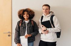 two people standing next to each other in front of a door and holding folders