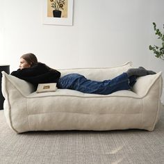 a woman laying on top of a white couch in a living room next to a potted plant