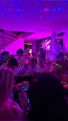 a group of people standing around each other in a room with purple lights on the ceiling