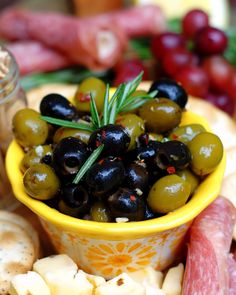 a yellow bowl filled with olives next to crackers and other food on a table