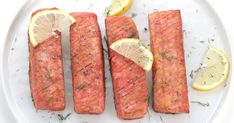 four pieces of salmon on a white plate with lemons and dill garnish