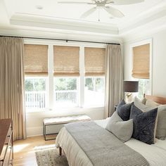 a bed sitting in a bedroom next to a window with roman shades on the windowsill