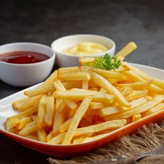 french fries with ketchup and mustard on a plate next to dipping sauces