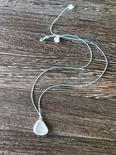 a white necklace on a wooden table with a cord and two small pendants hanging from it