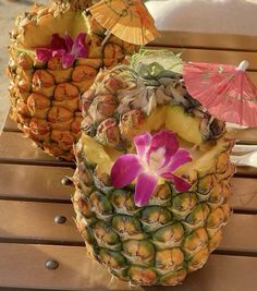 two pineapples with flowers and umbrellas on a wooden table in the sun