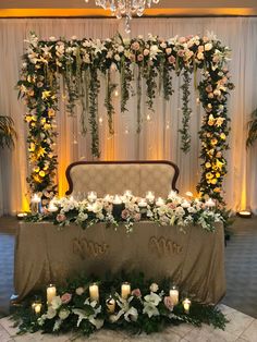 a table with candles and flowers on it in front of a wall decorated with greenery