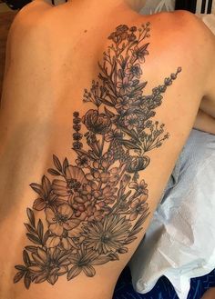 a woman's back with flowers and leaves tattoo on her left side ribcage